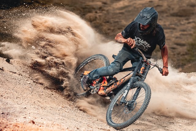 Downhill rider carving a berm with a big dust roost — Mottolino Bikepark, Livigno